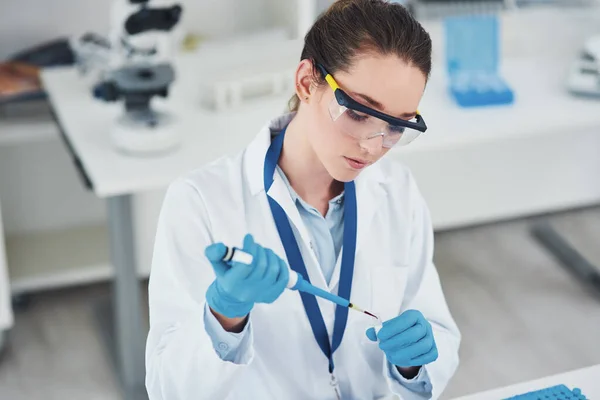 stock image One more drop to go. a focused young female scientist wearing protective glasses while pouring a test sample into a vile inside of a laboratory