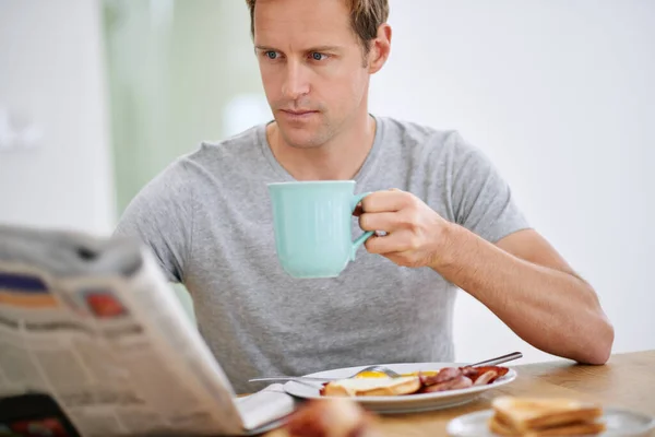 让我们看看世界上发生了什么 一个英俊的男人一边吃早饭一边看报纸 — 图库照片