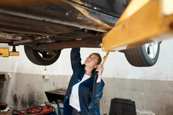 何年もあなたの車を走らせるのを手伝うことができます 解除された車の下で働く女性整備士は — ストック写真