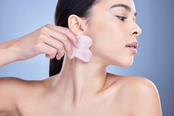 stock image A beautiful mixed race woman using a rose quartz gua sha to reduce wrinkles and promote cell renewal. Young hispanic woman using anti ageing tool against blue copyspace background.