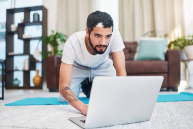 Çeşitli egzersiz videolarına erişimim var. Evde yoga yaparken laptopunu kullanan bir adam.