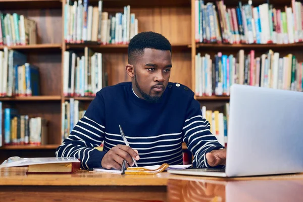 Library, laptop and university student with research, learning and planning for exam, report or focus on computer, studying or education. Black man, college and working on task, essay or scholarship.
