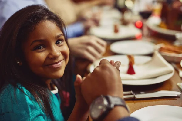 stock image Portrait, meal and girl with her family, prayer and happiness with joy, home or religious. Face, young person or female child holding hands, praying and worship for blessing, food or social gathering.