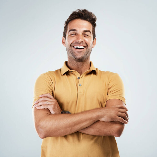 Im listening to you. Portrait of a cheerful young man smiling brightly with his arms folded while standing against a grey background