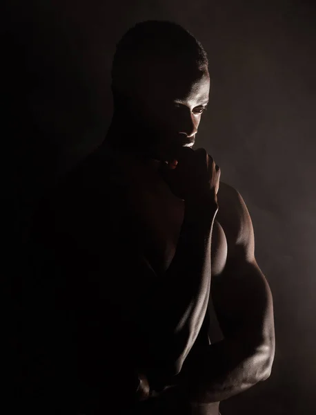 Black man, muscle silhouette and studio for thinking, anxiety and depression with art deco vision. Model, art aesthetic and depressed with strong body, alone or suffering with mental health in shadow.