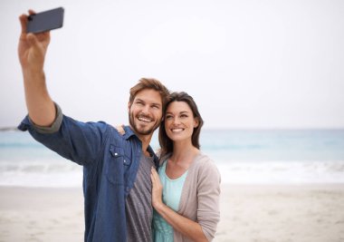 Aşk, selfie ve çift sahilde kucaklaşır. Birlikte gezmek, fotoğraf çekmek ve dışarıda özgürlük için. Gülümseyin, kucaklayın ve seyahat edin nüfuzlu insanlar blog, takipçiler veya sosyal medya profili resmi için canlı yayında.