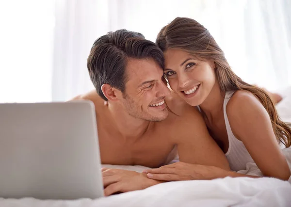 stock image Laptop, love and happy couple lying in bed together while watching a online movie or video at home. Happiness, smile and portrait of a woman browsing the internet on computer with husband in bedroom