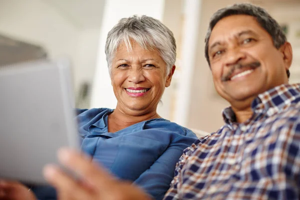 技術的な時代を受け入れる 家庭で一緒にデジタルタブレットを使って幸せな高齢者のカップルは — ストック写真