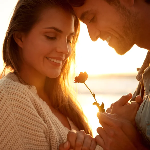 あなただけのために特別な何か 彼のガールフレンドに日没時にビーチで花を与える若い男 — ストック写真