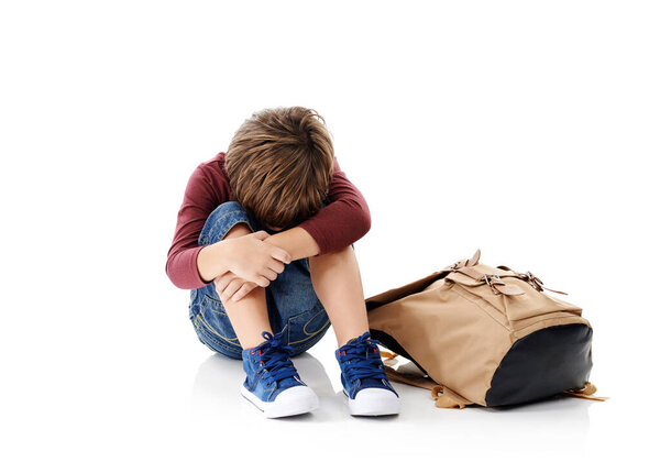 The first day of school can be challenging. Studio shot of a little boy with his head buried in his knees sitting next to his schoolbag against a white background
