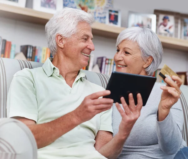 Stock image Senior couple, tablet and credit card for online shopping on living room sofa together at home. Happy elderly man and woman smiling on technology for ecommerce, banking app or payment on lounge couch.