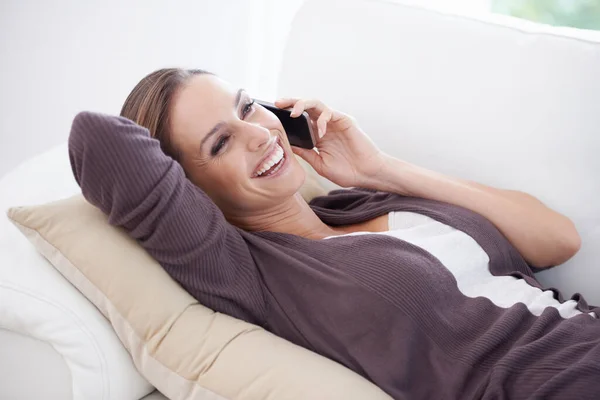 stock image Its great to hear from you. A young woman lying on her couch speaking on her cellphone
