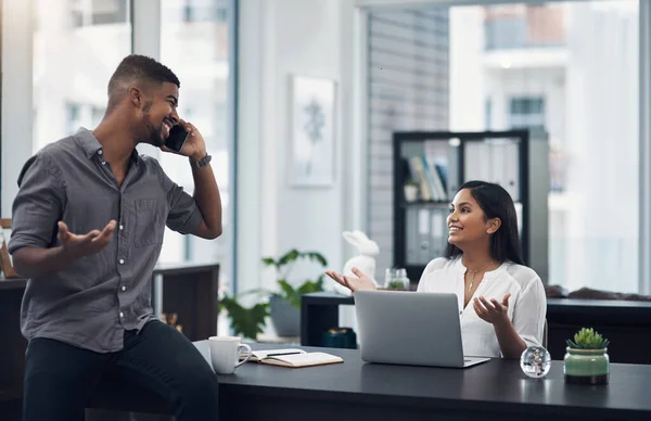 Did we get the deal or not then. a young businessman talking on a cellphone while his colleague is shrugging at her in an office