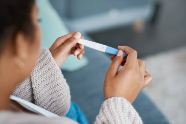Hamilelik testi, kadın eli ve oturma odasındaki kanepede sonuçları beklemek. Ev, kadın ve eli tıbbi ve doğurganlık testi çubuğuyla yalnız başına kanepede hamilelik işaretini gösteriyor..