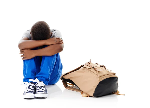 stock image I dont want to. Studio shot of a little boy with his head buried in his knees sitting next to his schoolbag against a white background