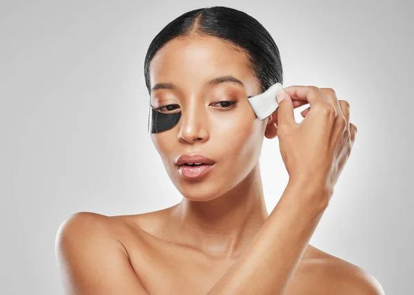 stock image Hydrating, soothing and cooling. Studio shot of an attractive young woman removing an under eye patch against a grey background