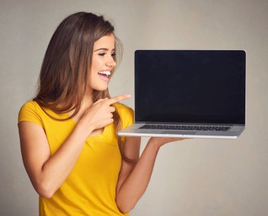 Anında ve daha hızlı internet erişimi sağla. Gri bir arkaplan üzerinde boş ekranı olan bir dizüstü bilgisayar tutan çekici genç bir kadın.