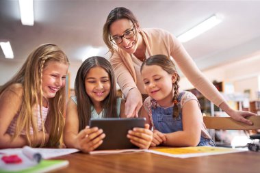 Modern çağlarda küçük beyinleri şekillendirmek. Okulda dijital tablet kullanan bir öğretmen öğrencilerine yardım ediyor.