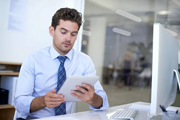 在设备之间同步他的数据 一位年轻的商人坐在办公桌前 一边用数字平板电脑 — 图库照片
