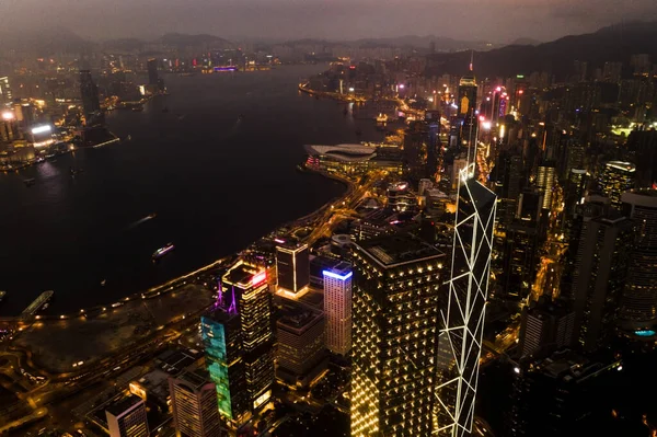 Aerial, skyscrapers and night city of office buildings with lake, lights and riverside in the outdoors. Drone view of CBD, architecture or cityscape and late infrastructure lighting of a urban town.