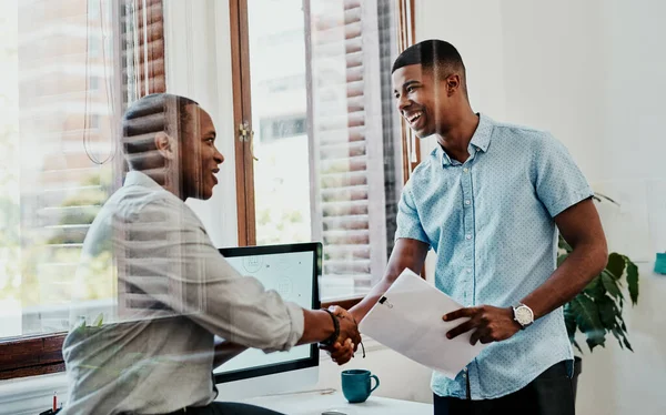 Pleasure doing business with you. two young businessmen shaking hands in a modern office