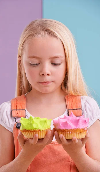 Hmm...which one is bigger. A cute little girl trying to decide which cupcake she should eat