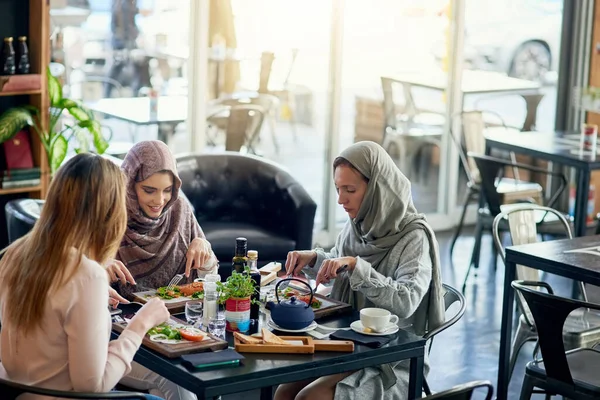 Muslim women, talking and lunch in restaurant, together or friends with food, smile or happiness. Islamic woman, hungry group and brunch with social conversation, eating or listening to chat in cafe.
