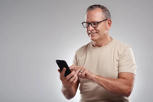 stock image Staying up to date on social media. a handsome mature man standing alone against a grey background in the studio and using his cellphone