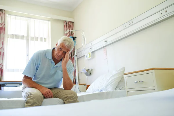 下一步是什么 一个老年人痛苦地一个人坐在医院病房的床上的画像 — 图库照片