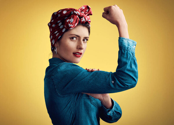Woman, strong and flexing muscle portrait of a pinup girl in studio for beauty, power and fashion. Female person show bicep on a yellow background for motivation, freedom and retro or vintage style.