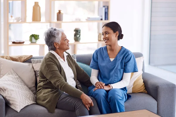 Healthcare, retirement and a nurse talking to an old woman on a sofa in the living room of a nursing home. Medical, trust and care with a female medicine professional chatting to a senior resident.