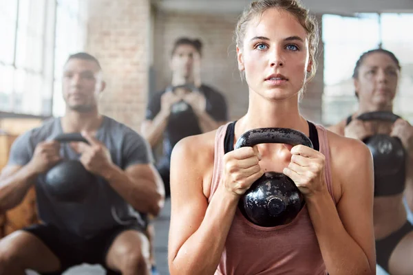 Fitness, exercise and woman with kettlebell in a gym for a strength training challenge. Sports, energy and female athlete doing a workout with weights with her friends or community in wellness center.