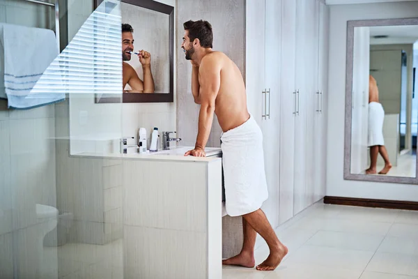 stock image Man brushing teeth in bathroom at mirror for dental wellness, healthy habit and gums. Shirtless guy, shower and cleaning mouth for fresh breath, oral hygiene and morning routine for grooming at home.