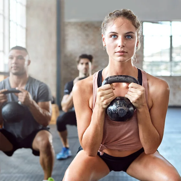 Sports, kettlebell and woman doing a workout with a group for strength training in a gym. Fitness, energy and female athlete doing a exercise challenge with weights with people in a wellness center