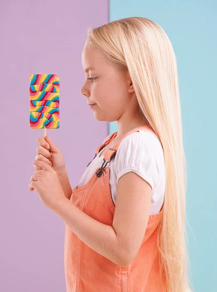 康德等着吃一口 一个可爱的小女孩拿着棒棒糖 面对着一个五颜六色的背景 — 图库照片