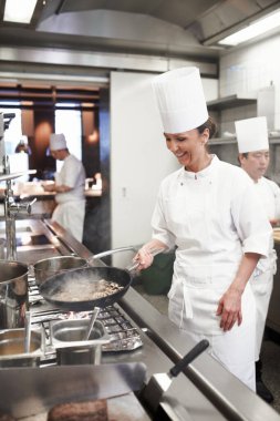 Şef, kadın ve restoranın mutfağında kızartma, yemek servisi ve güzel yemekler. Profesyonel, aşçı ve kadın eti tavayla soteler, konukseverlik için yemek yapar..