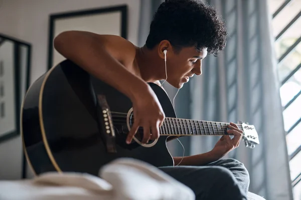 どんな感じかな 家でギターを弾きながらイヤホンを使っている若い男が — ストック写真
