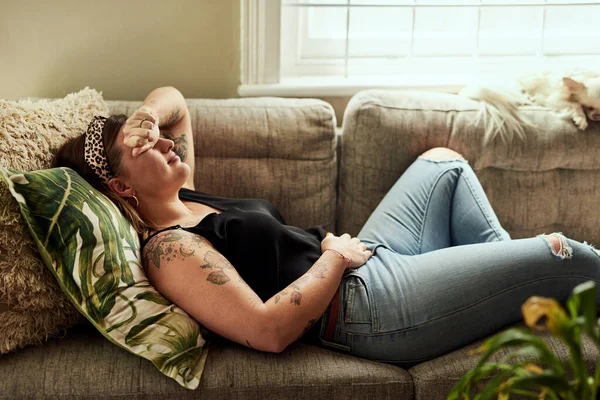 stock image Period pain, menstruation and a woman on a sofa in the living room of her home suffering from cramps. Stomach, digestion and constipation with a young female person holding her belly in discomfort.