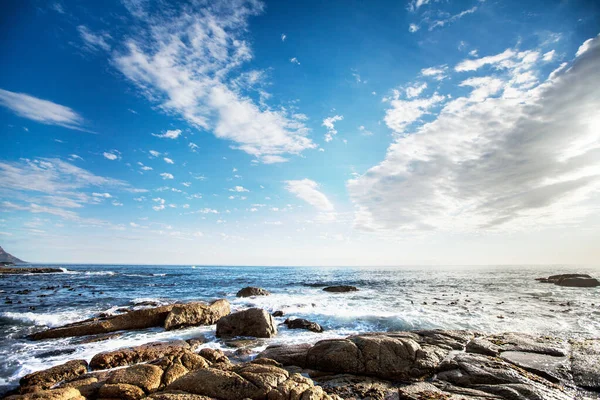 stock image Rock, ocean and nature with waves at beach for environment, landscape and blue sky. Calm, summer and seascape with sunrise on horizon at coastline for tropical, clouds and water surface.