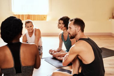 Elinden gelenin en iyisini yapanlarla birlikte ol. Yoga dersi sırasında sohbet eden bir grup genç erkek ve kadın.