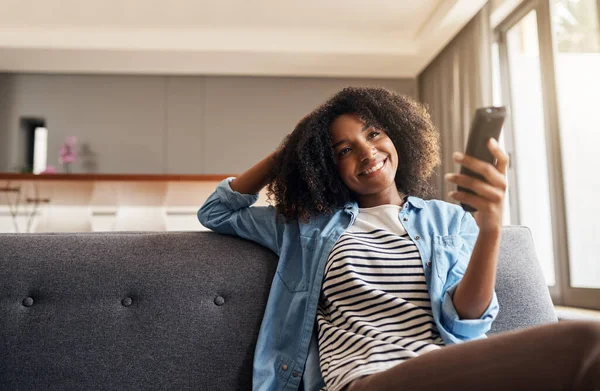stock image Relax, black woman with remote and watching tv on sofa in living room of her home. Entertainment or comfort, streaming movie or a series and happy African female person watch television on a couch.