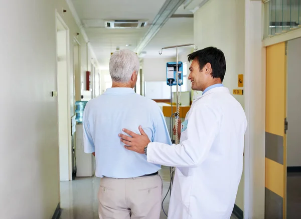 stock image Dont get your wires crossed now. a handsome young doctor walking with his senior patient down the hall