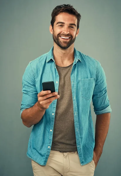 社会的存在として つながりを保つことが重要です 灰色の背景を持つ携帯電話を使用してハンサムな若い男のスタジオの肖像画 — ストック写真