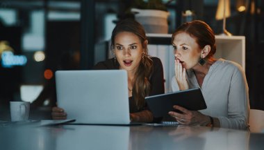 Success goes beyond the 9-5. two businesswomen looking surprised while working together on a laptop in an office at night clipart