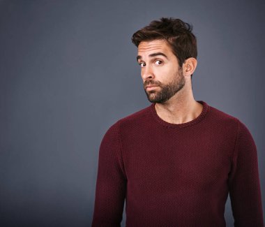 Im not sure I believe you. Studio shot of a handsome young man looking skeptical against a gray background