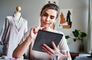 İnternet ilham doludur. Bir moda tasarımcısı atölyesinde otururken dijital tablet kullanıyor.