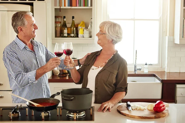 Cheers, happy or old couple cooking food for a healthy vegan diet together with love in retirement at home. Smile, toast or senior woman drinking wine in kitchen to celebrate with husband at dinner.