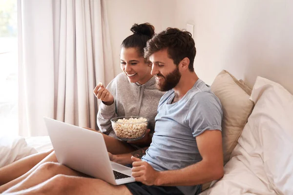 stock image Watching movie, popcorn and couple in bed with laptop for streaming, food and internet. Subscription, happy and comic with man and woman at home for social media, funny and free time on weekend.