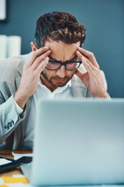 Gerilim baş ağrıları gününüzü yavaşlatabilir. Ofiste dizüstü bilgisayar üzerinde çalışırken stresli görünen genç bir işadamı.