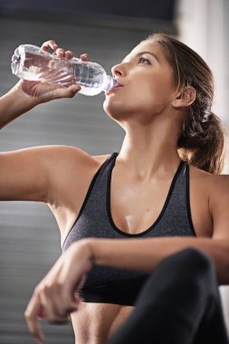 Susuz kalmamak çok önemli. Spor salonunda su şişesinden su içen genç bir kadın.